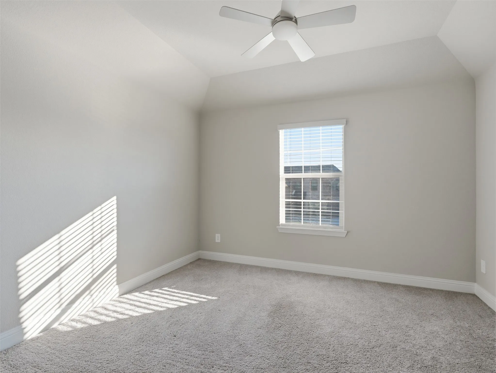 Vaulted ceiling, ceiling fan, single window with blinds, light gray wall paint, and gray carpet flooring