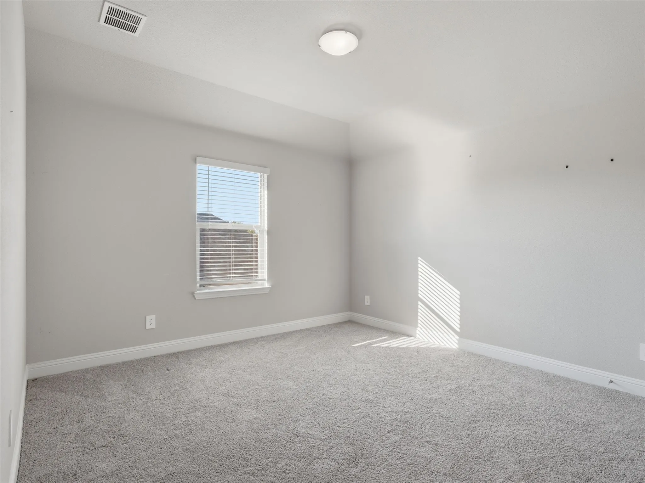 Bright, spacious bedroom flooded with natural light through a large window with plantation shutters