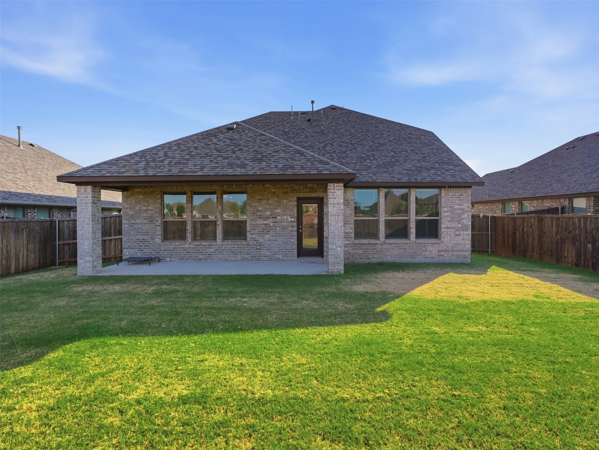 Expansive backyard with a covered patio, brick exterior, multiple windows, and a wood privacy fence