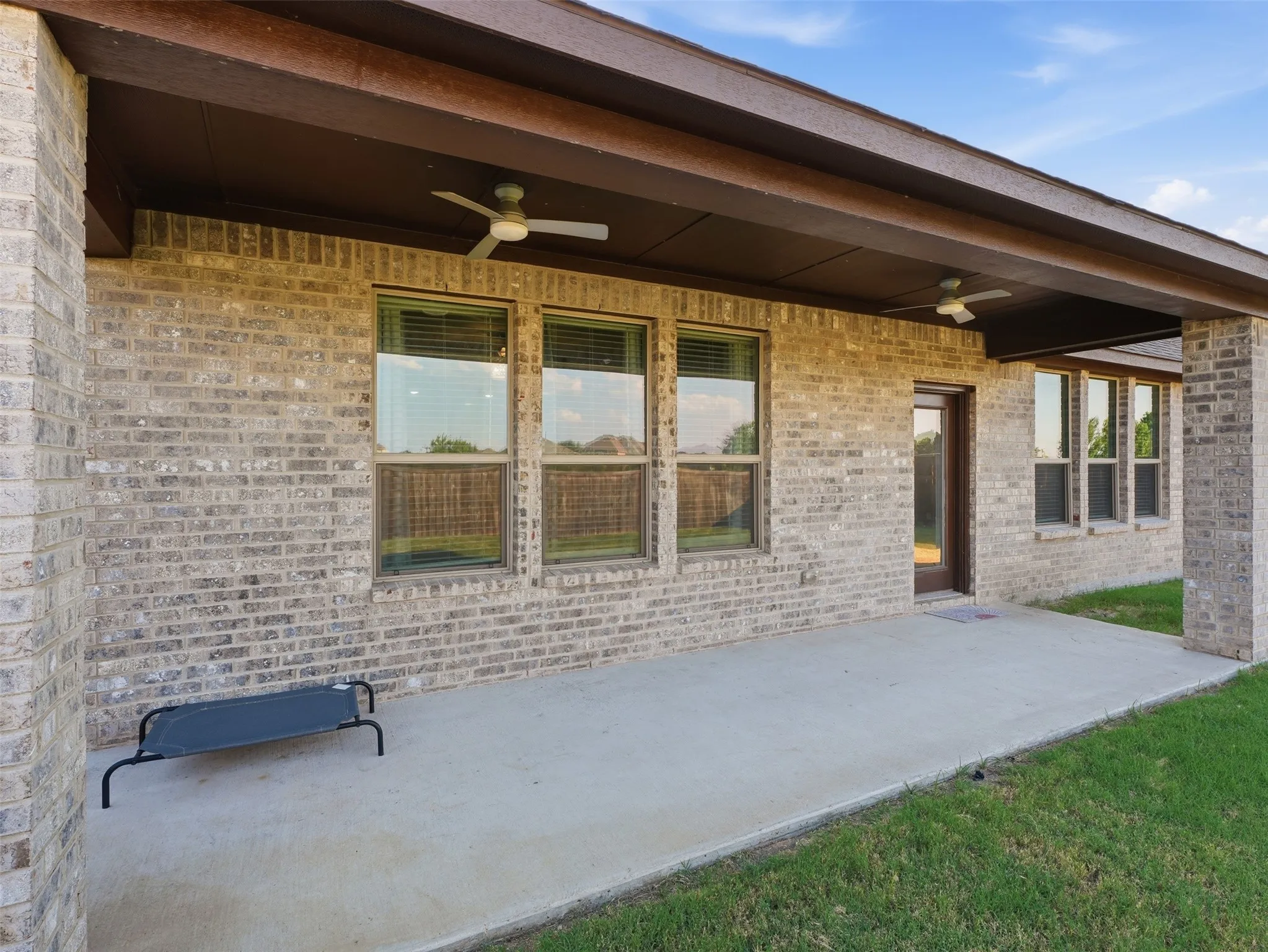 Modern brick exterior with expansive covered patio featuring concrete flooring, ceiling fans, and abundant natural light from triple-pane windows