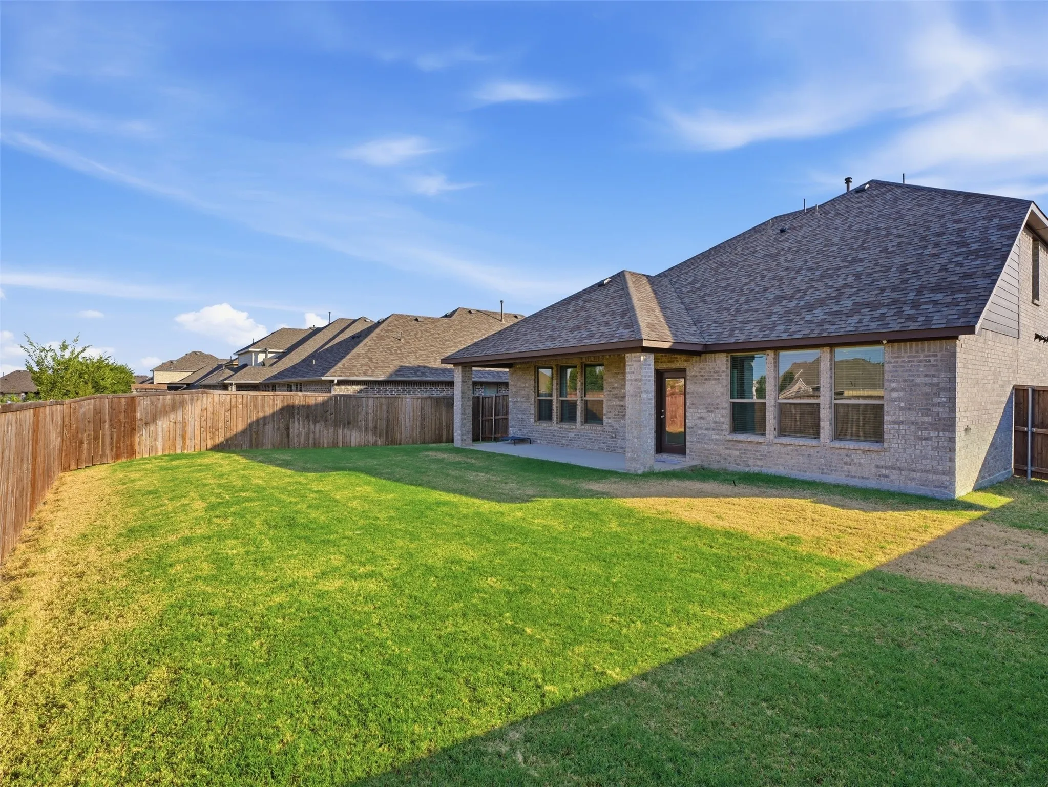 Expansive backyard with a manicured lawn, full privacy fencing, a covered patio, and a brick exterior