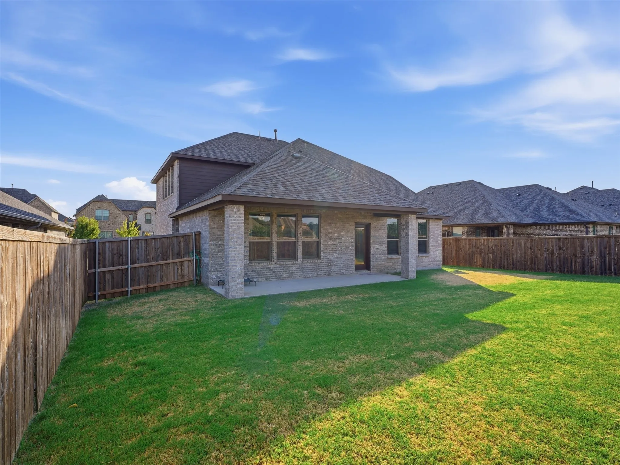 Brick exterior with covered patio, wood fencing, and a grassy backyard