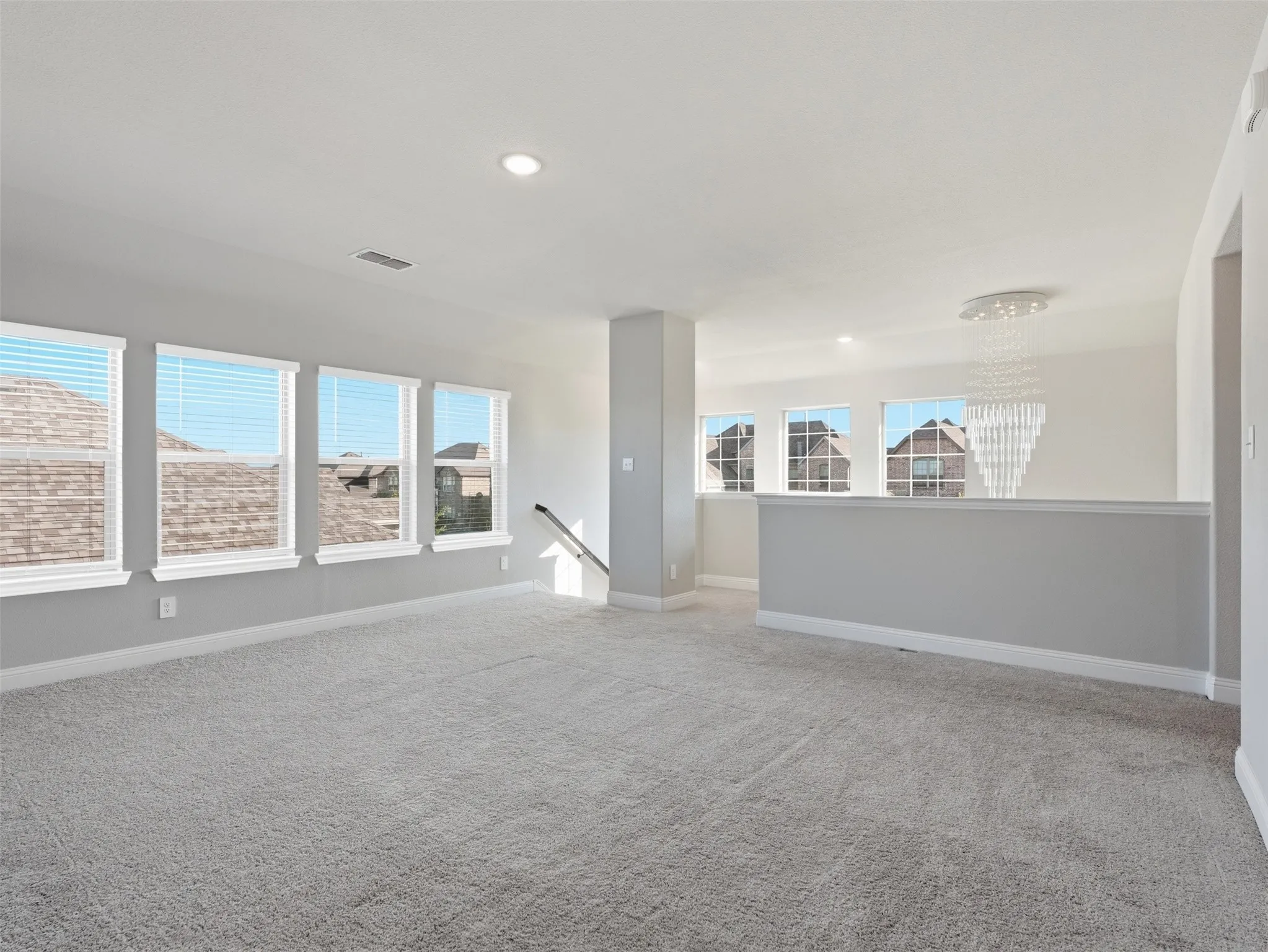 Carpeted upstairs bonus area featuring multiple windows with blinds, recessed lighting, and a contemporary chandelier