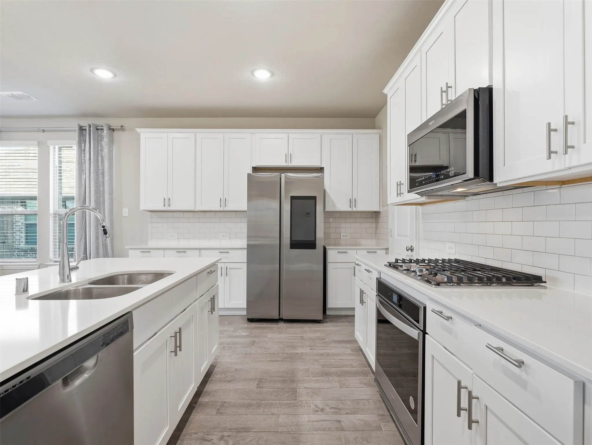 Modern kitchen featuring white cabinetry, stainless steel appliances, a gas range, a double basin sink, and wood-finish flooring