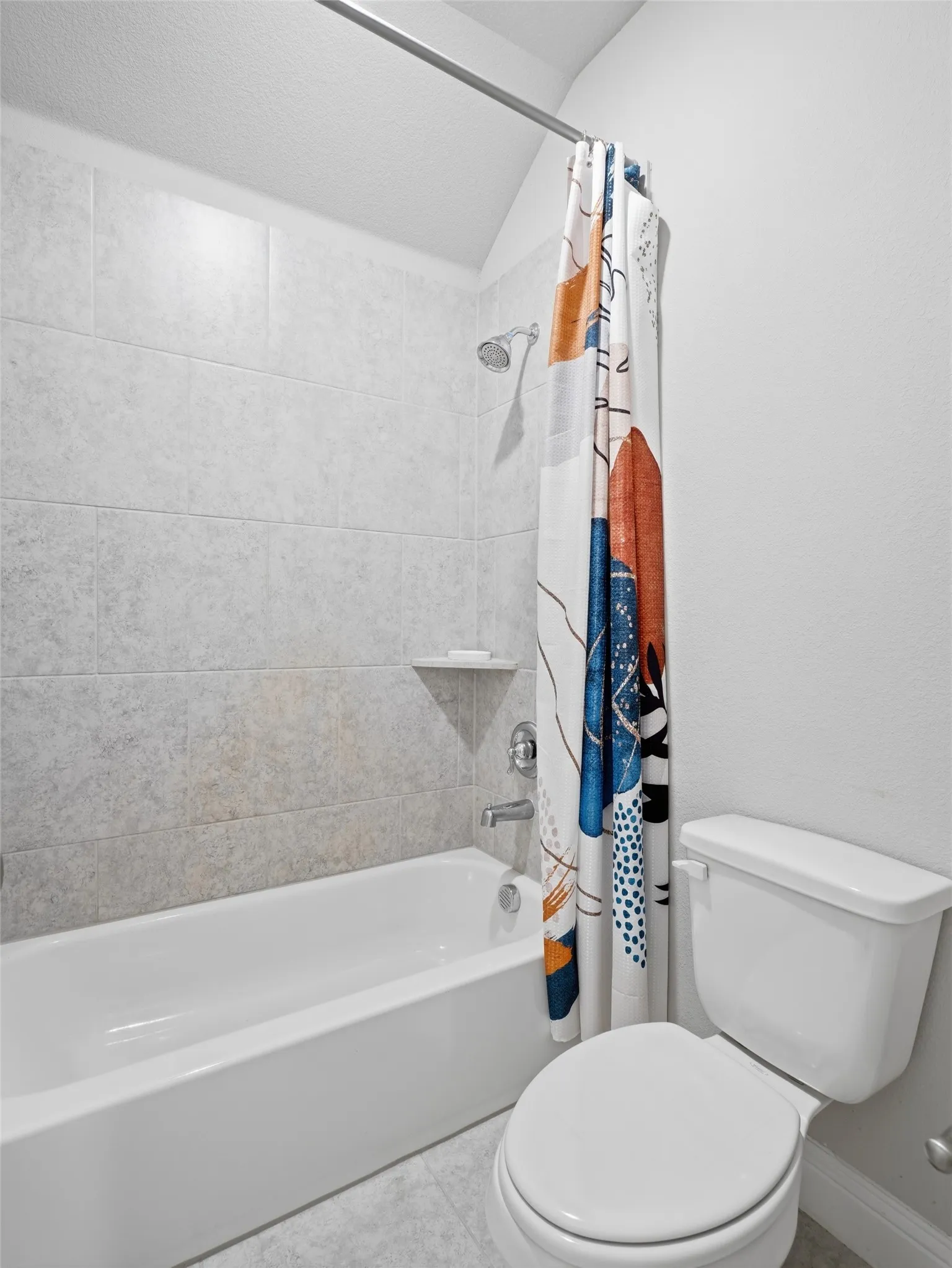 White porcelain bathtub and toilet, light-toned wall tile, and a built-in shower niche