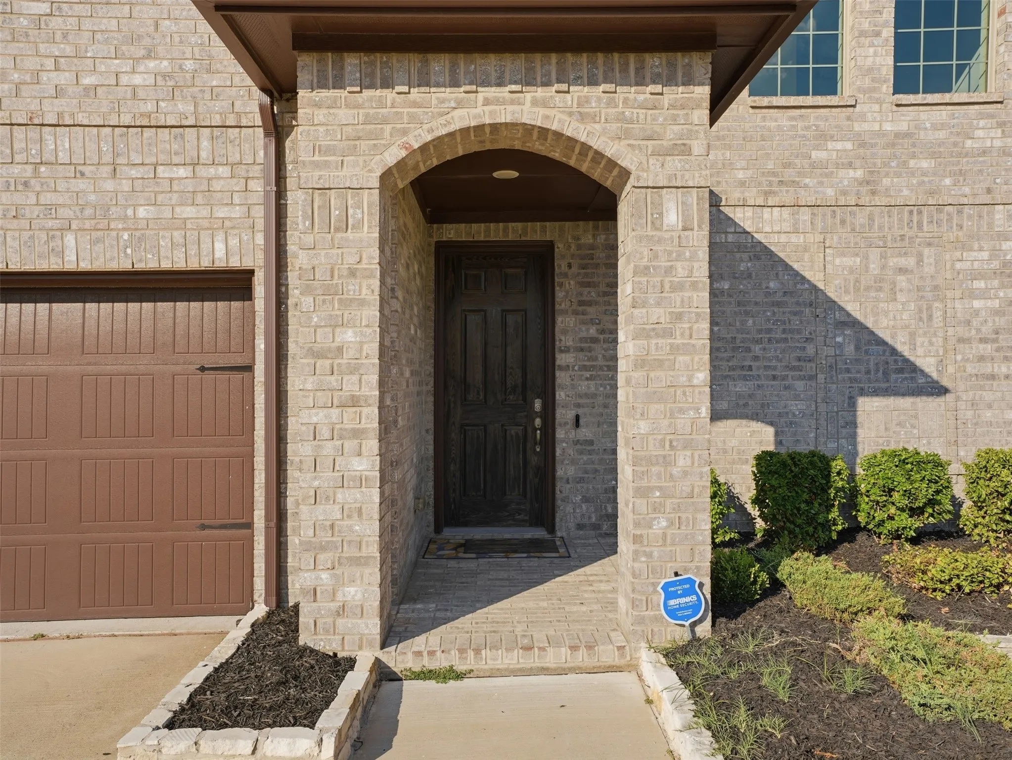 Brick exterior with an arched entryway, paneled front door, and an attached garage