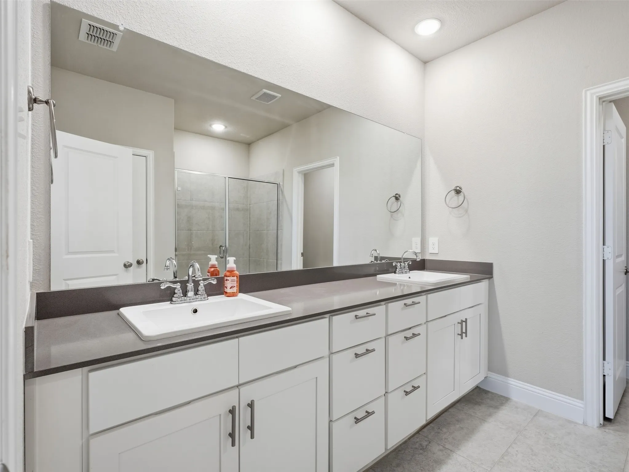 Dual sink vanity with white cabinetry, dark gray countertop, and an expansive mirror