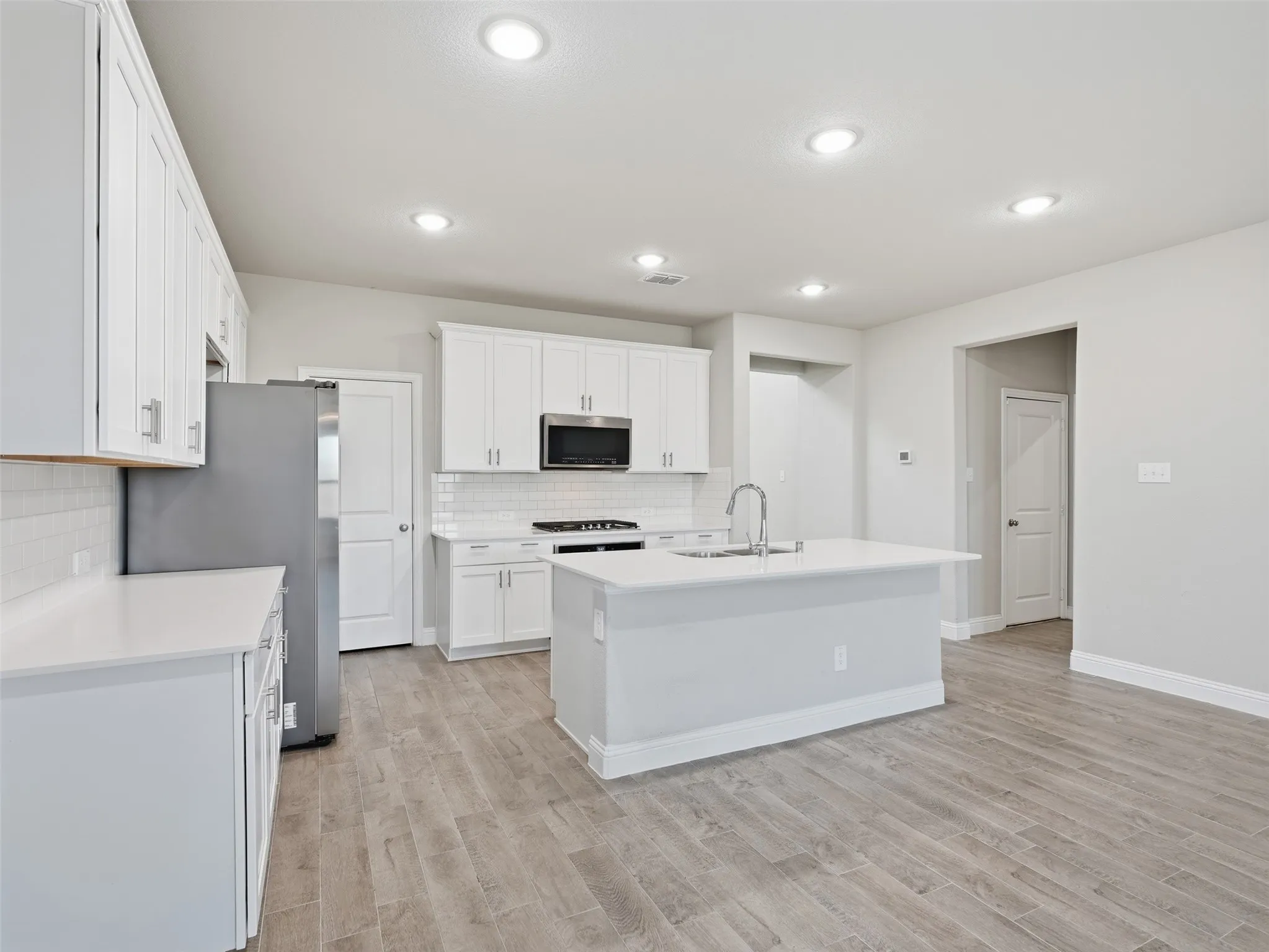 Kitchen featuring white cabinetry, light-toned countertops, a center island with sink, stainless steel appliances, and wood-finish flooring