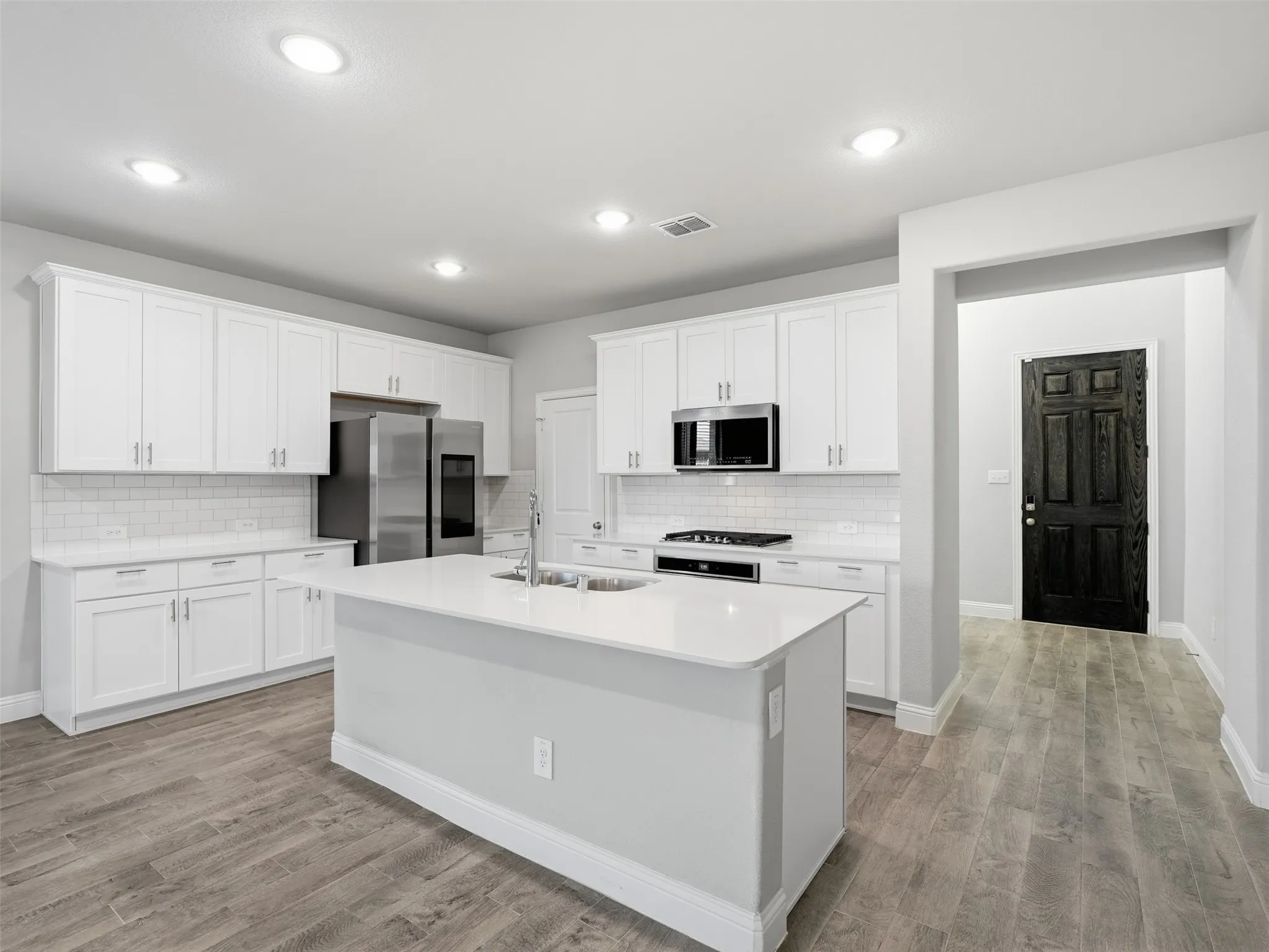Kitchen featuring an island with an integrated sink, white cabinetry, stainless steel appliances, white subway tile backsplash, and wood-finish flooring