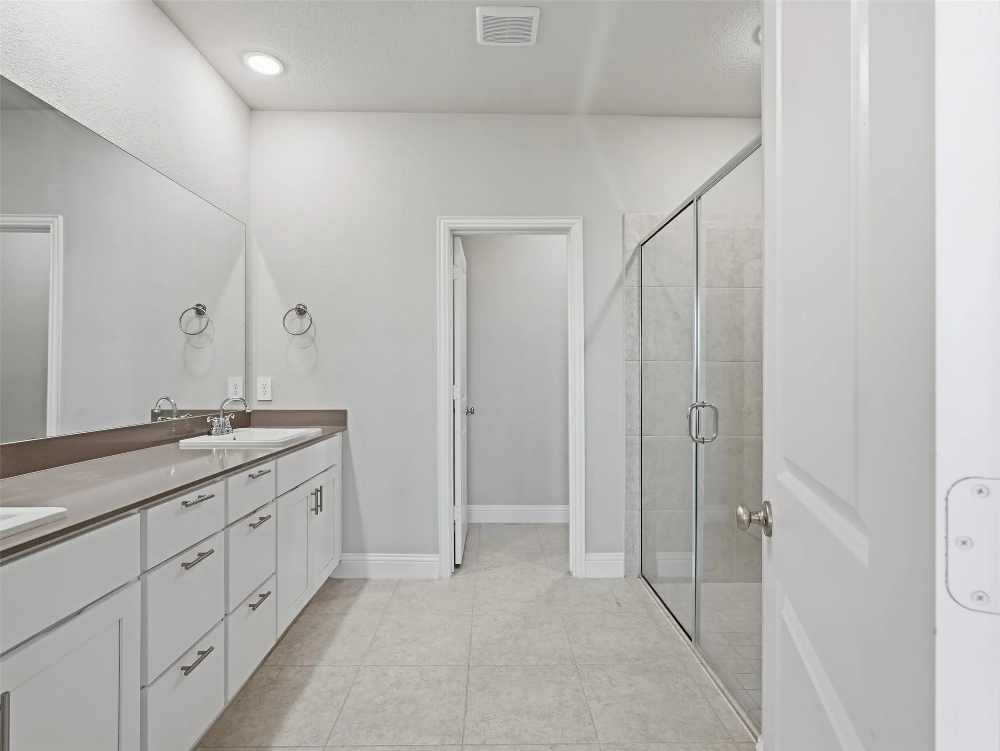 Dual vanity with integrated sinks, expansive mirror, walk-in shower with glass enclosure, tile flooring, and recessed lighting