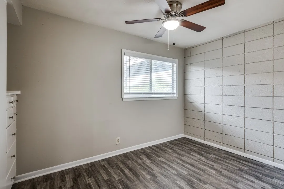 Wood-finish flooring, textured accent wall, ceiling fan with light fixture, window with blinds, and built-in cabinetry