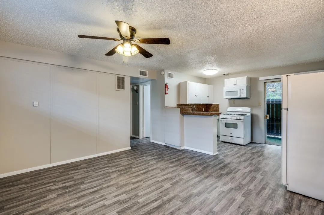 Open-concept living area featuring wood-finish flooring, a ceiling fan, and an integrated kitchen with white cabinetry, a gas range, and a refrigerator