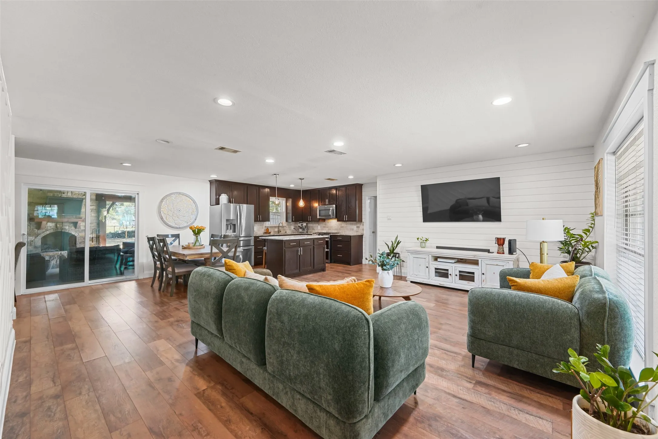 Open-concept living area featuring warm wood-finish flooring throughout, recessed ceiling lighting, and built-in entertainment cabinetry with media display