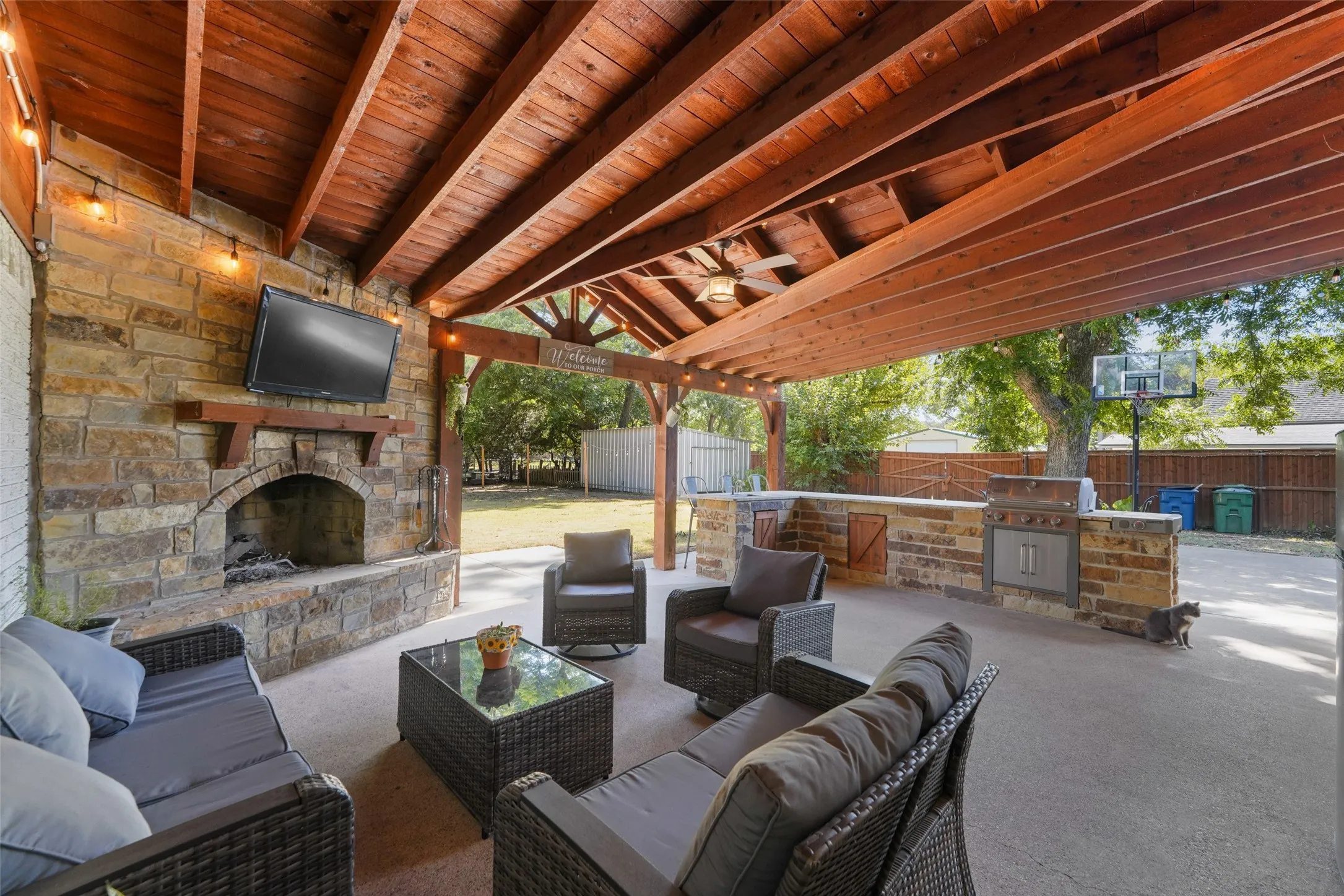 Covered patio featuring a wood-plank ceiling, stone fireplace with mantel, built-in outdoor kitchen, and ceiling fan