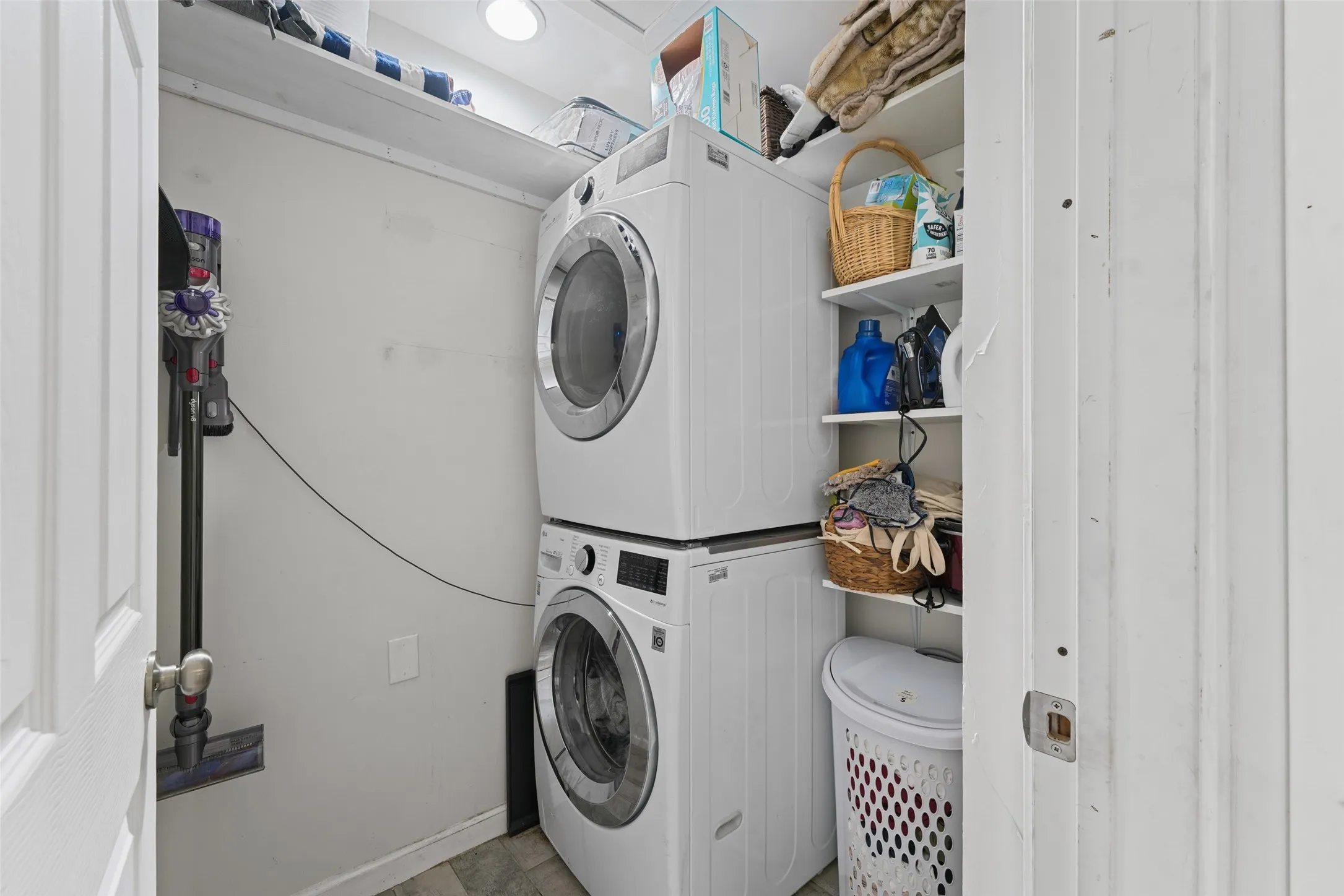 Dedicated laundry area featuring a stacked washer and dryer, built-in shelving, and overhead lighting