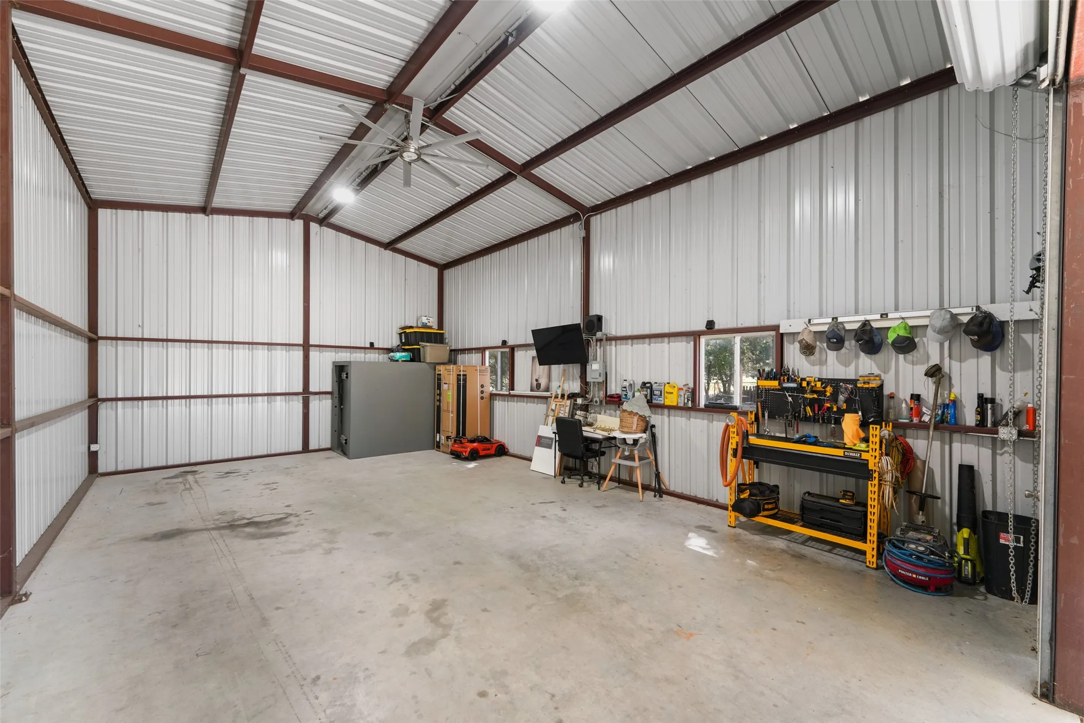 Spacious metal building with a concrete floor, exposed beam ceiling, large ceiling fan, and multiple windows