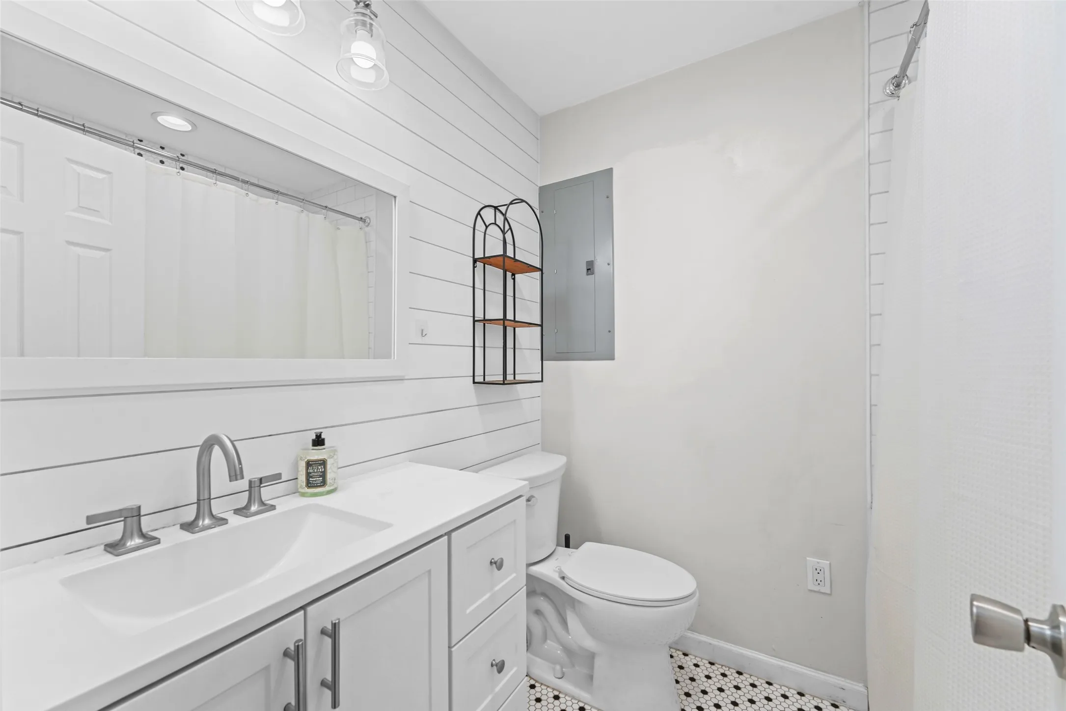 Vanity with integrated sink, brushed nickel faucet, wall-mounted mirror, and decorative wall paneling