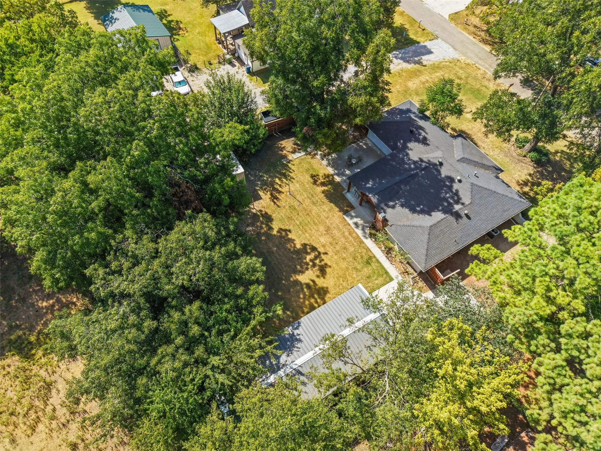 Residential property featuring a dark shingle roof, mature perimeter trees, and an expansive lawn