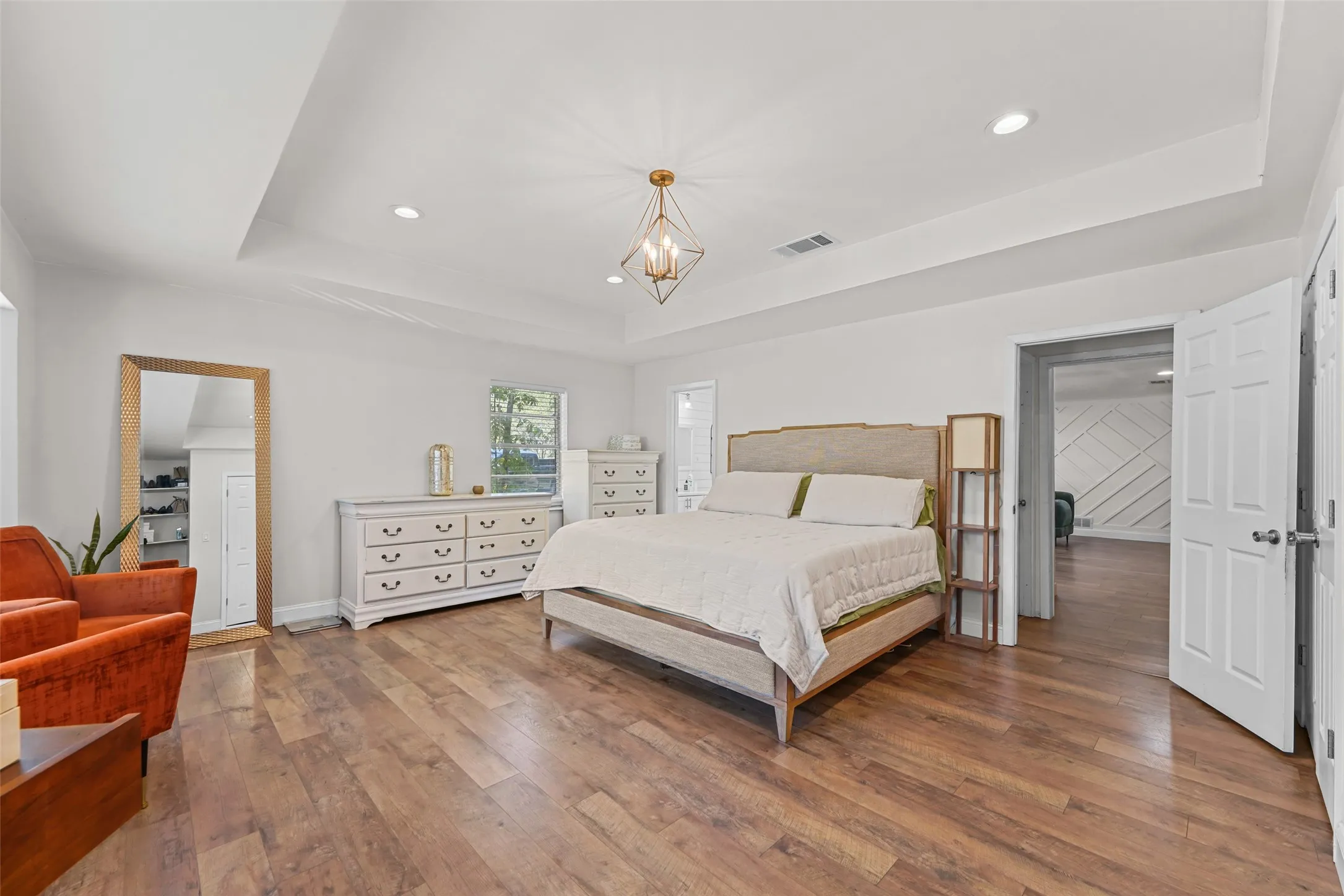 Tray ceiling with recessed lighting, wood-finish flooring, and a modern chandelier