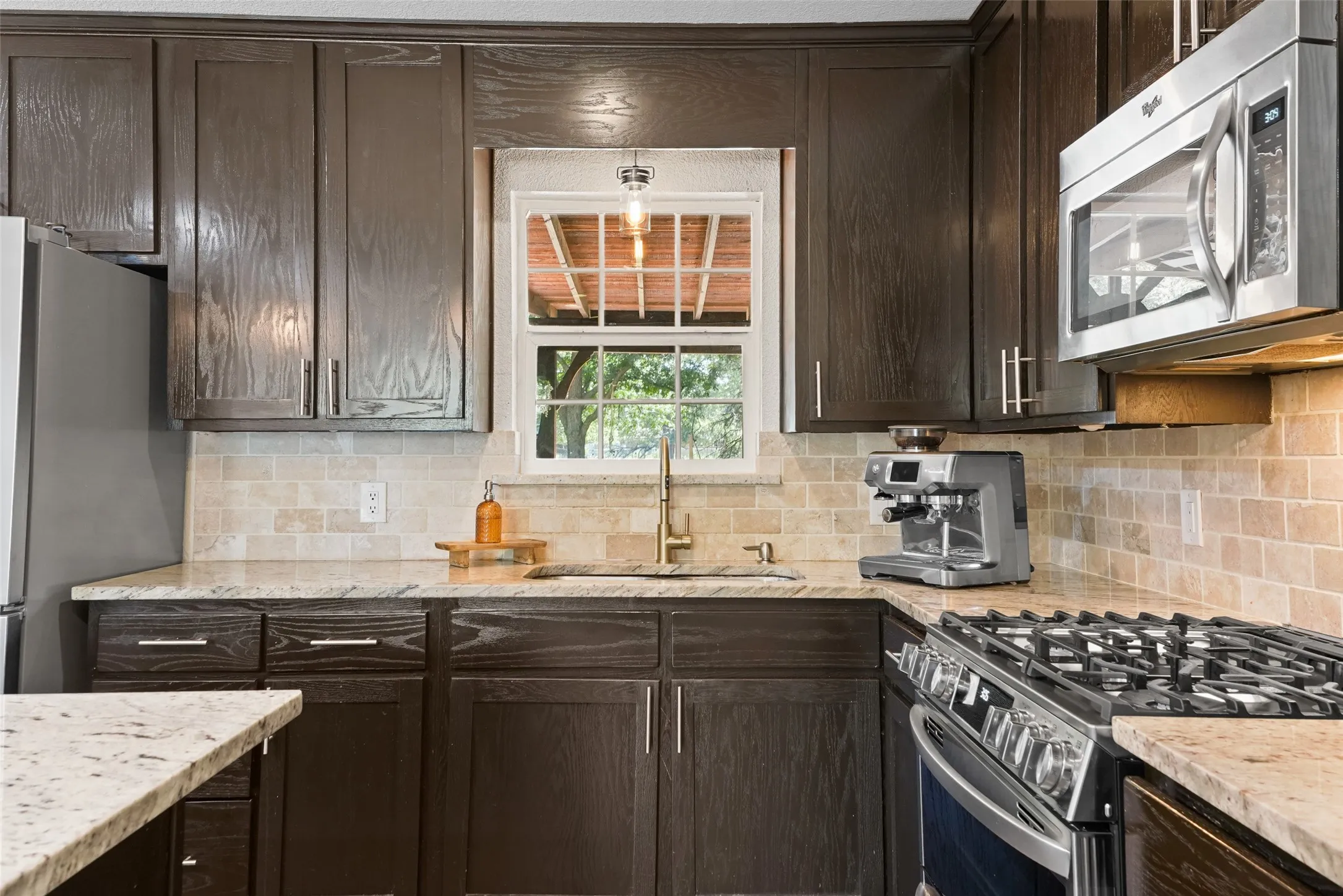 Kitchen featuring wood-finish cabinetry, light-toned countertops, a tile backsplash, stainless steel appliances, and a gas range