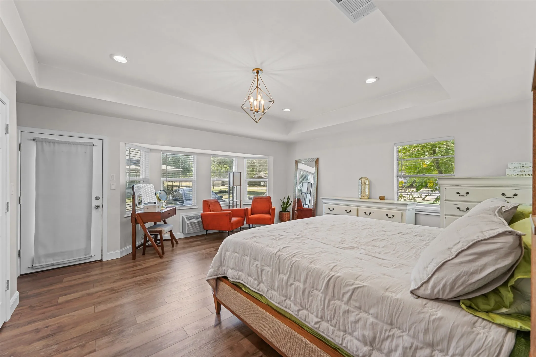Tray ceiling with recessed lighting, wood-finish flooring, bay window, and a geometric chandelier