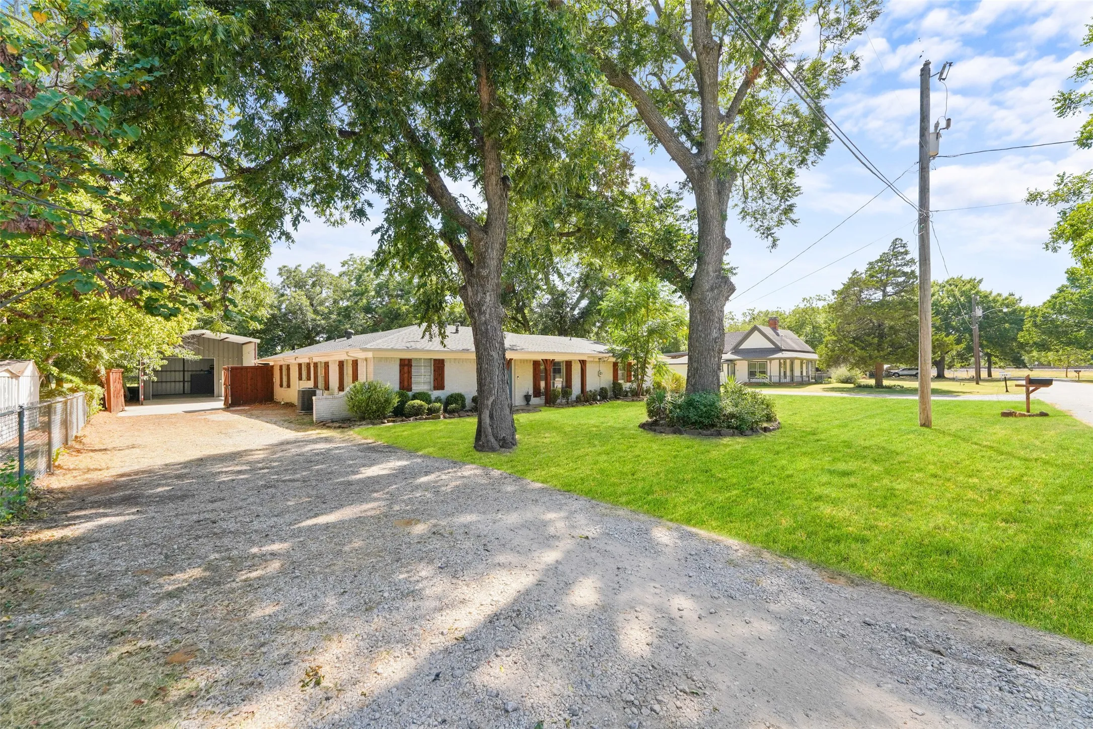 Ranch-style residence with a gravel driveway, mature trees, and a detached metal carport