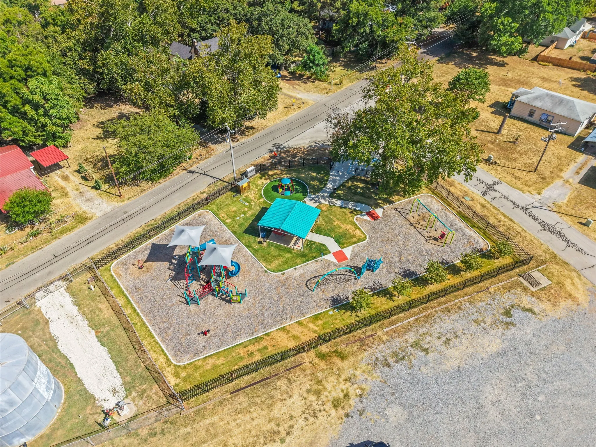 Fenced playground area featuring multiple play structures, swings, and a shaded picnic area