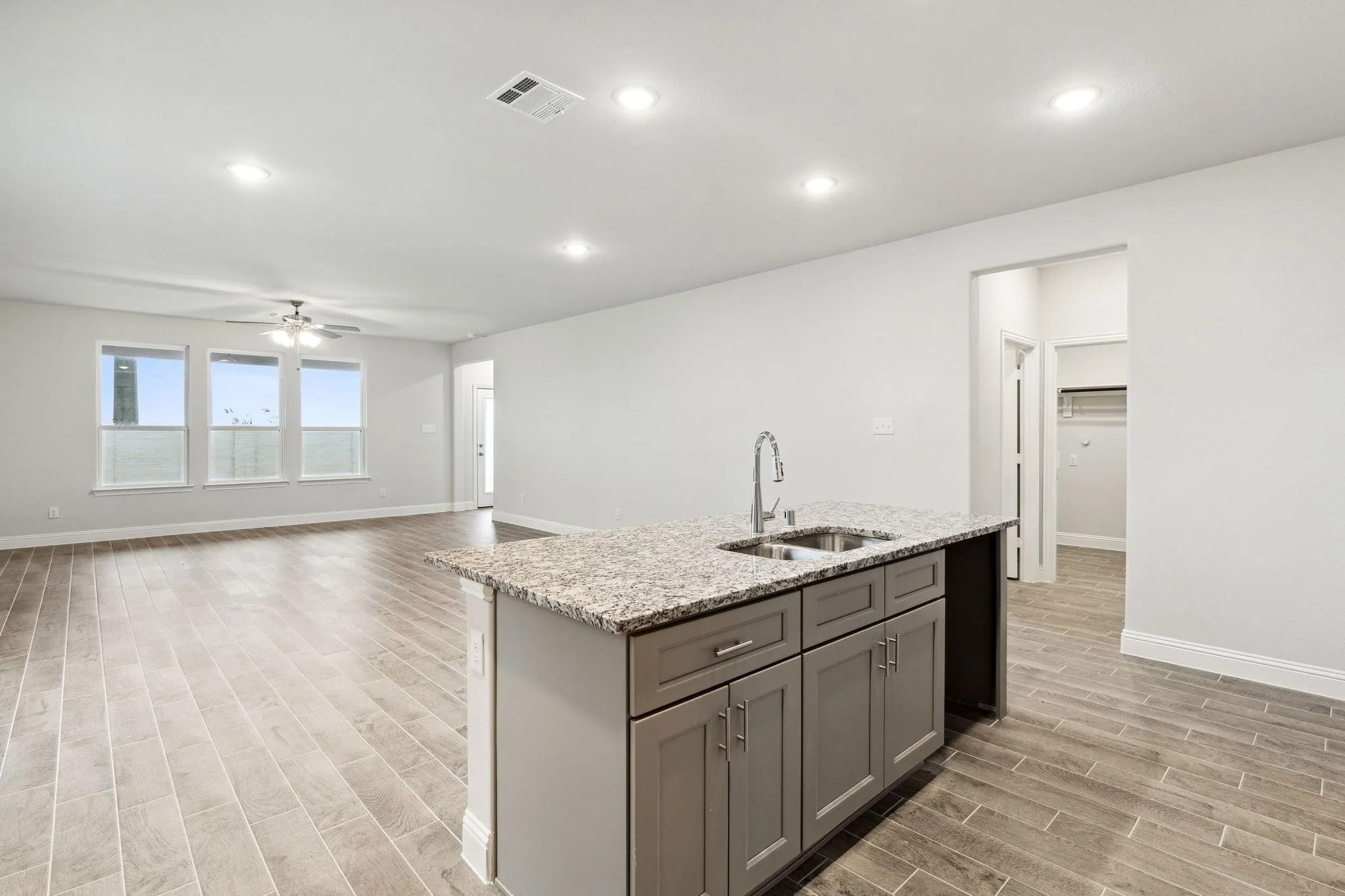 Kitchen with gray cabinetry, sink, an island with sink, light stone counters, and light hardwood / wood-style flooring