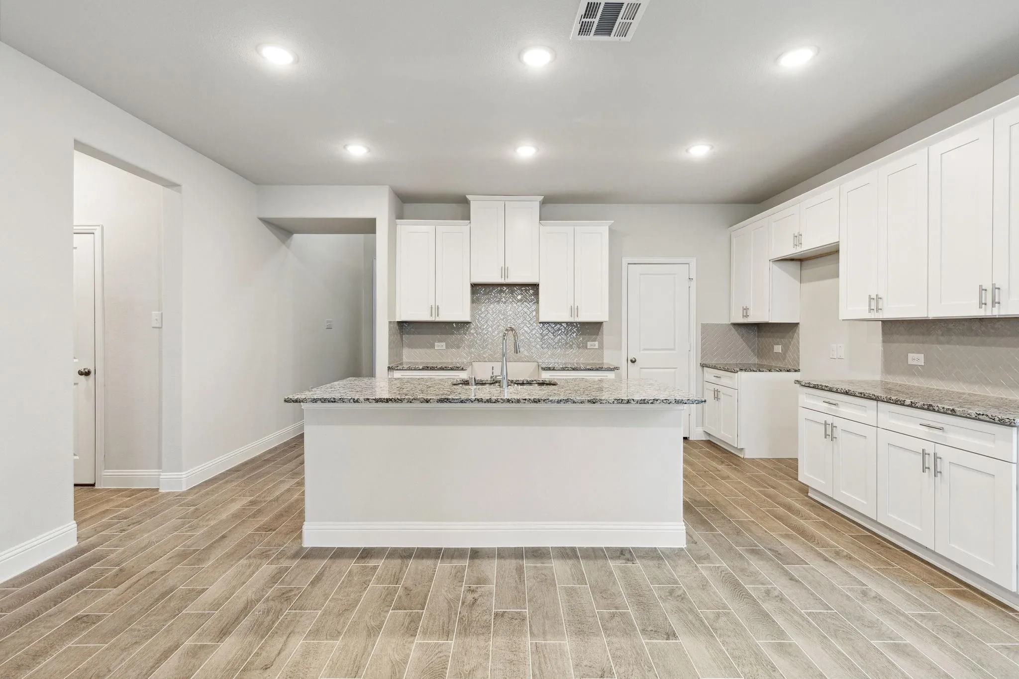 Kitchen with light hardwood / wood-style flooring, light stone counters, and a kitchen island with sink