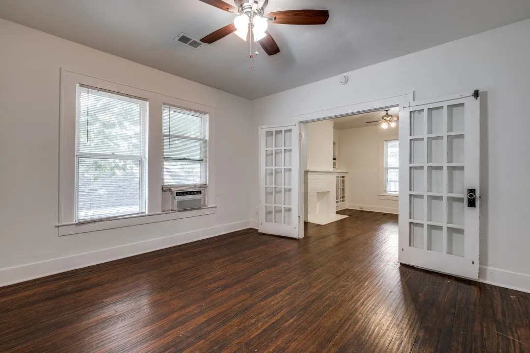 Dark wood-finish flooring, white walls, ceiling fan with light fixture, and white French doors with dark hardware