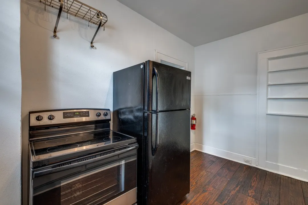 Stainless steel electric range, black refrigerator, wood-finish flooring, and built-in shelving