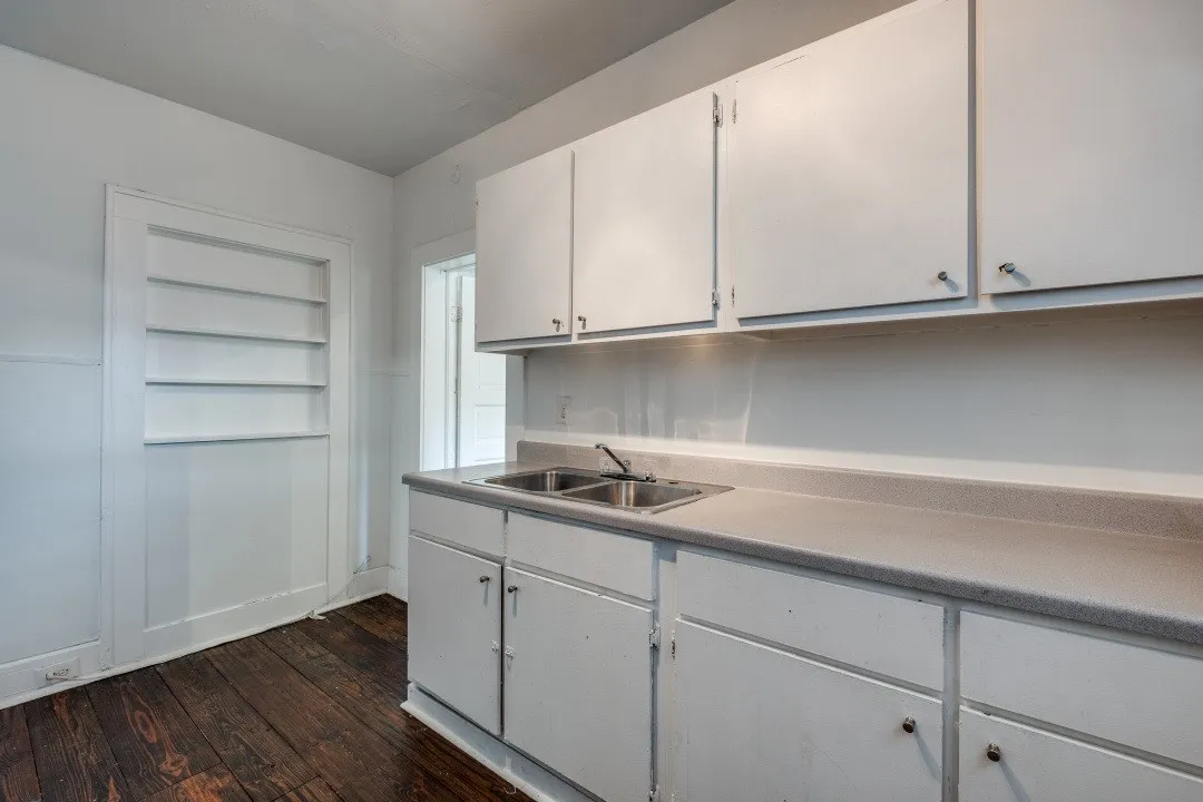 White cabinetry with chrome hardware, dual basin stainless steel sink, light-toned countertop, and built-in wall shelving