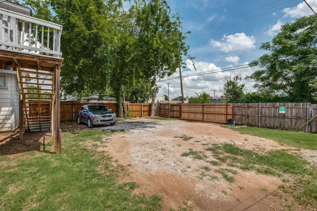 Private backyard featuring wood fencing, mature trees, and a gravel parking area