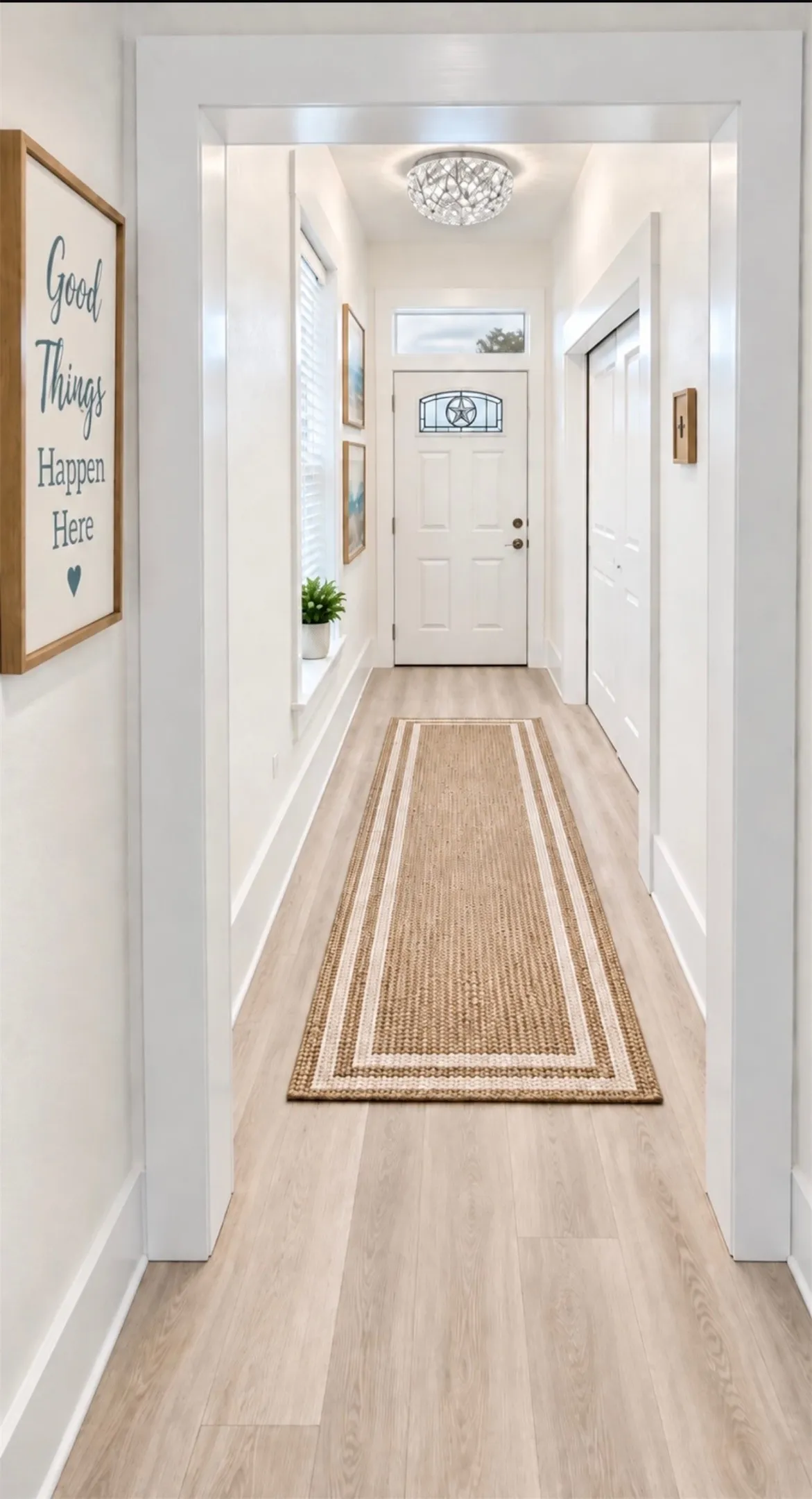 Light wood-finish flooring, white paneled door with decorative glass insert, transom window, and a crystal flush-mount light fixture