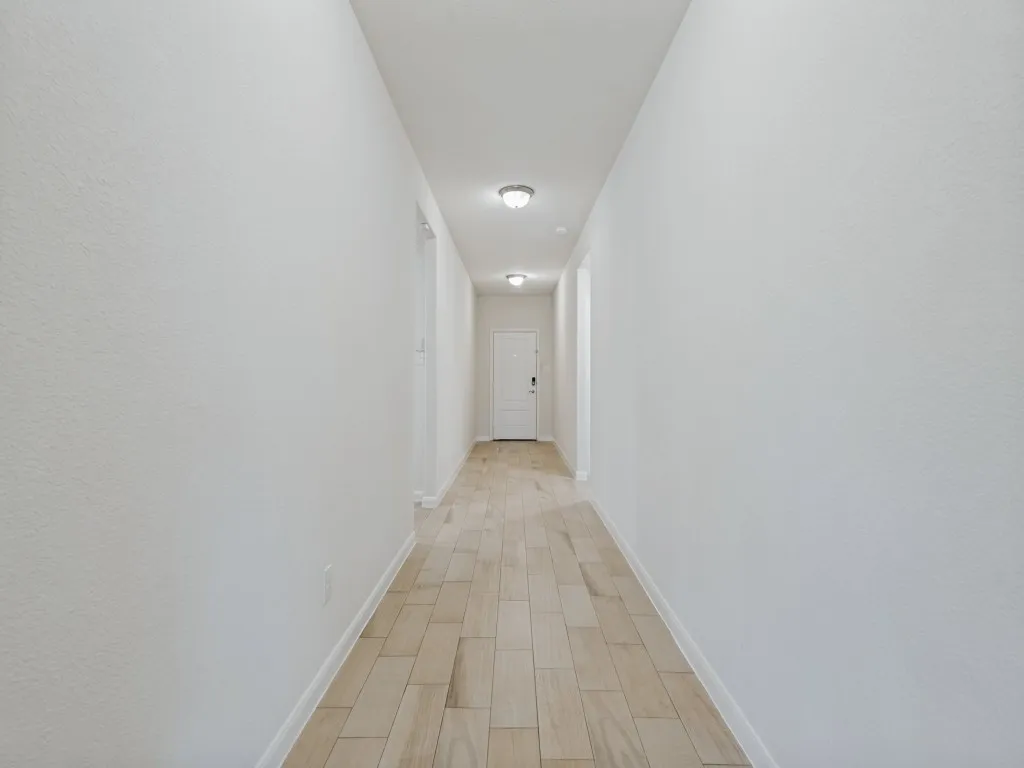 Light-toned wood-finish flooring extending through a bright hallway with recessed lighting