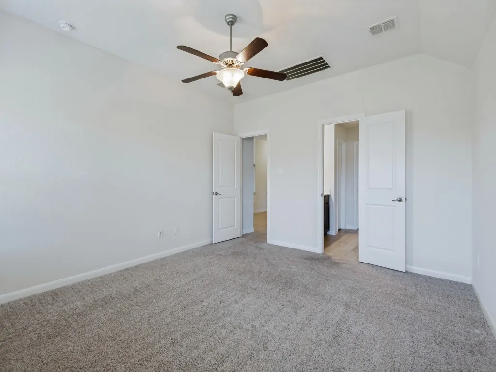 Vaulted ceiling with a ceiling fan light fixture, gray carpet flooring, and white paneled doors