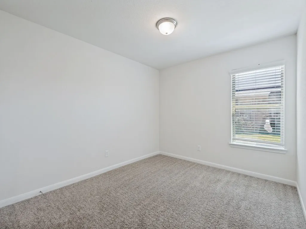 Neutral-toned carpeting paired with white walls, a single window with blinds, and a flush-mount ceiling light fixture
