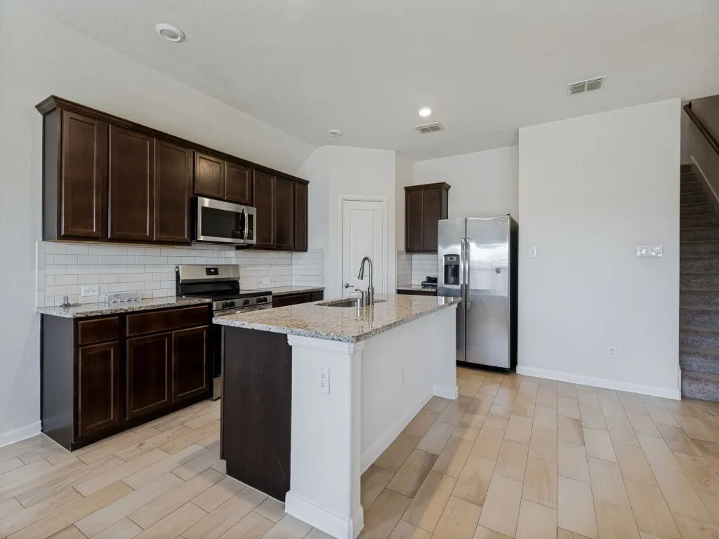 Kitchen featuring wood-finish flooring, dark wood cabinetry, stainless steel appliances, a tile backsplash, and an island with a countertop