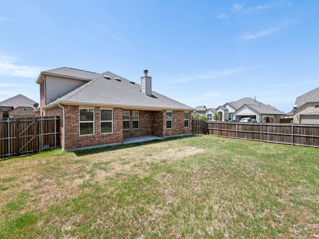 Expansive backyard with a wood privacy fence, brick exterior, and covered patio