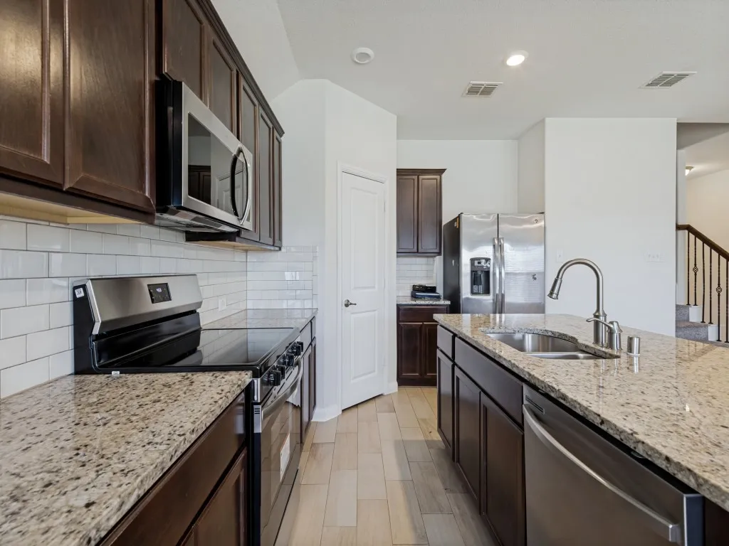 Kitchen featuring dark wood-finish cabinetry, light speckled countertops, stainless steel appliances, and a subway tile backsplash
