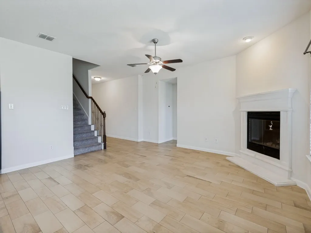 Light wood-finish flooring, white walls, and a fireplace with a white mantel and hearth