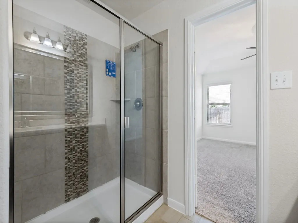 Glass-enclosed shower with a tiled surround featuring an accent mosaic strip