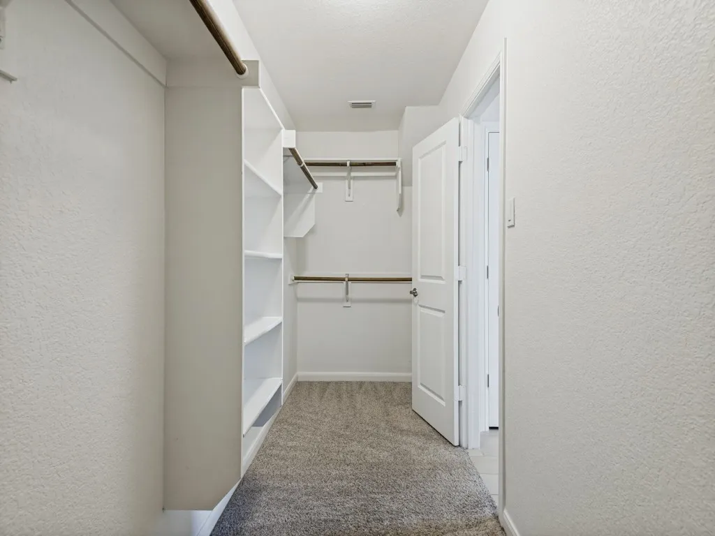 Spacious walk-in closet featuring multiple built-in shelving units, dual clothing rods with brass hardware, and neutral carpeting throughout
