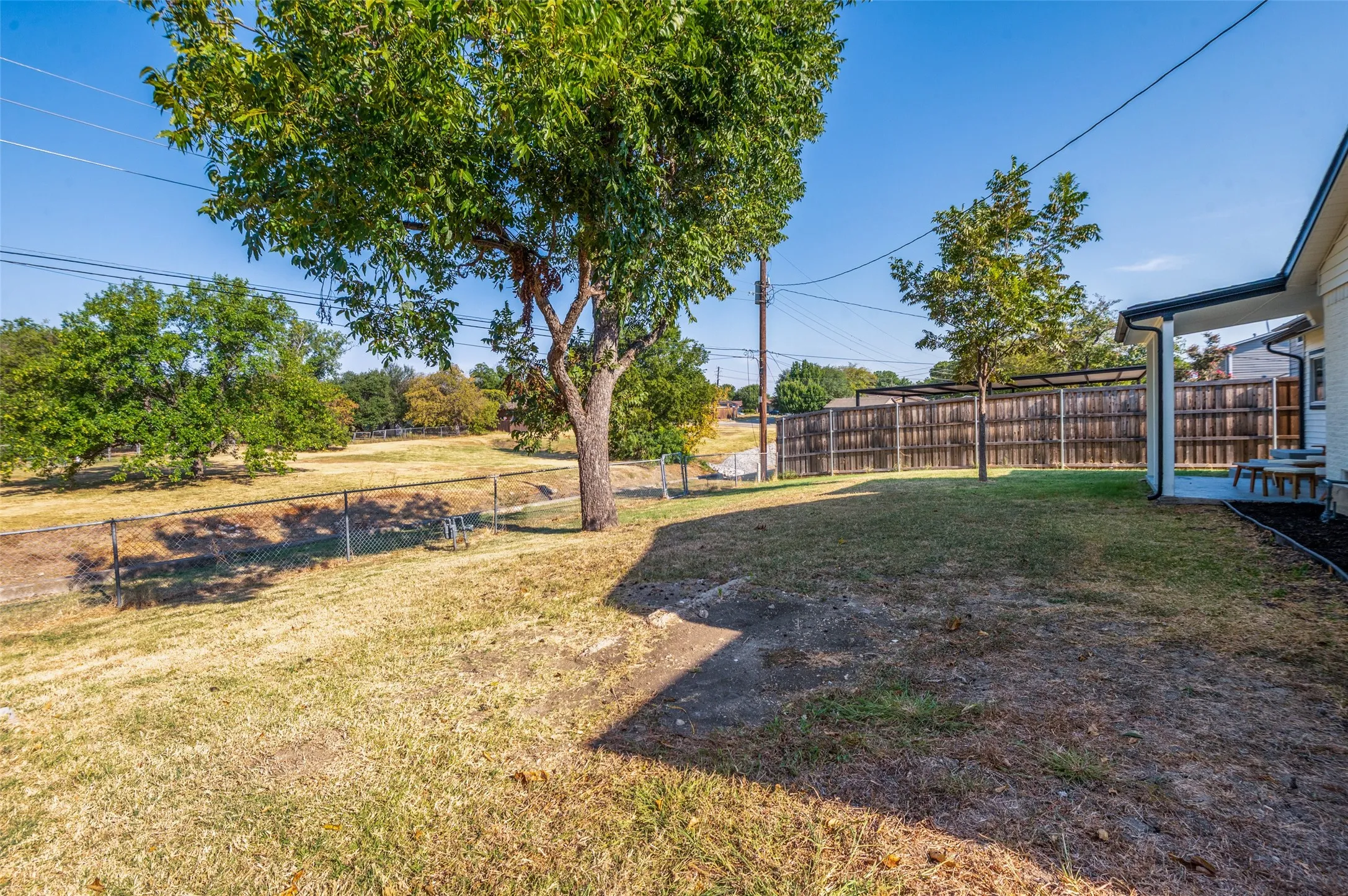 Spacious backyard featuring a covered patio, established trees, and wood privacy fencing