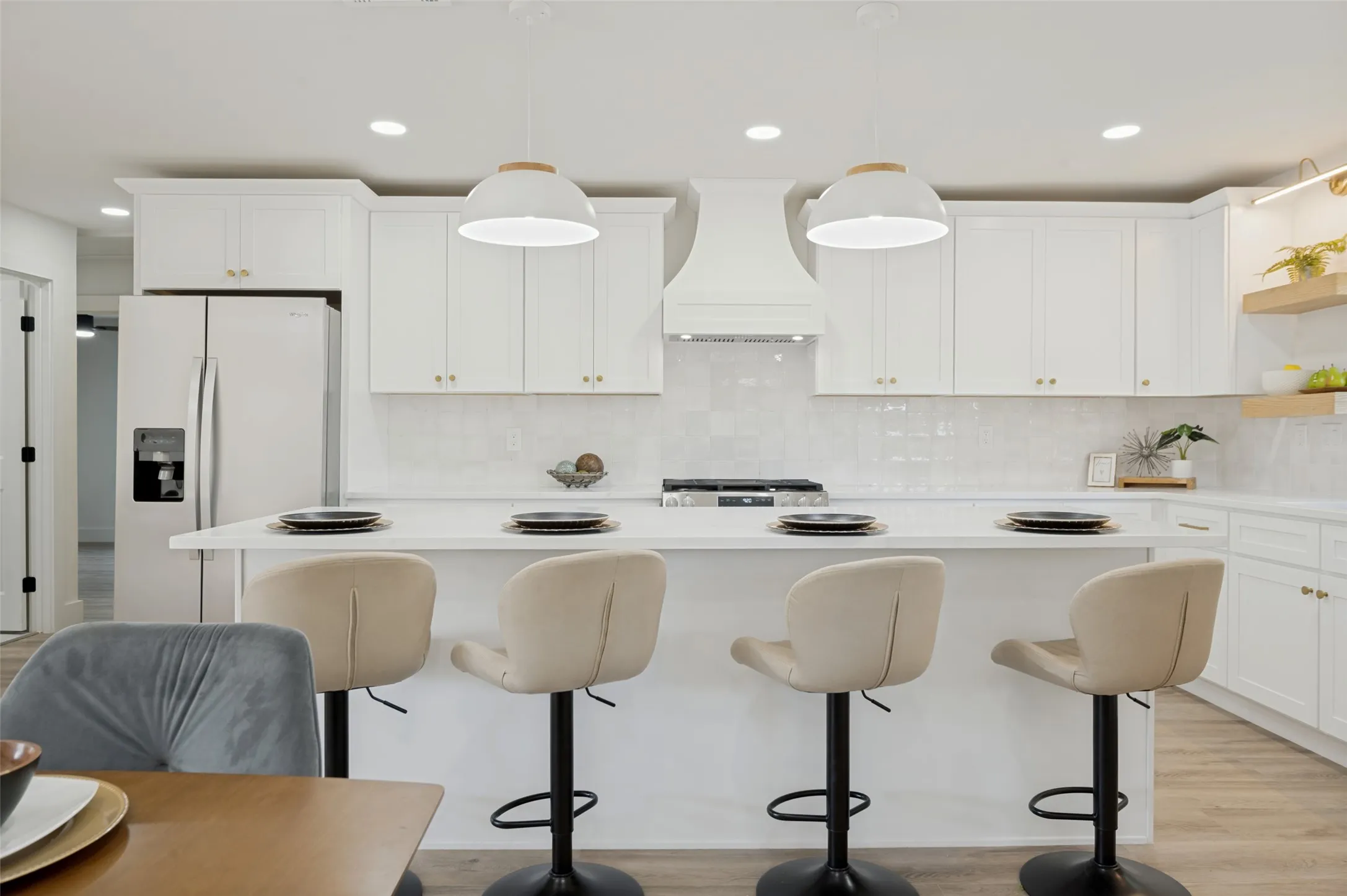 Kitchen featuring white cabinetry, a large center island, built-in range hood, white tile backsplash, and light wood-finish flooring