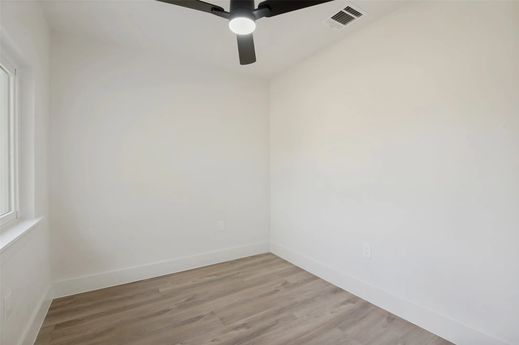 Wood-finish flooring, white walls, modern ceiling fan with integrated lighting, and a white-framed window