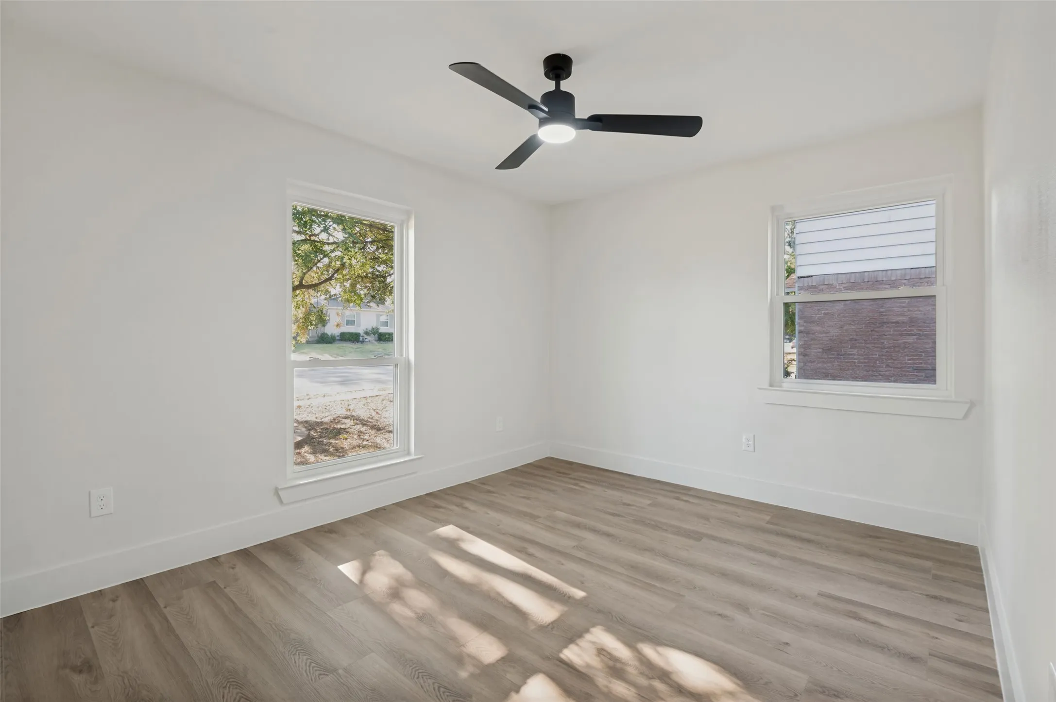 Neutral white wall paint, two windows, wood-finish flooring, and a modern ceiling fan with integrated lighting
