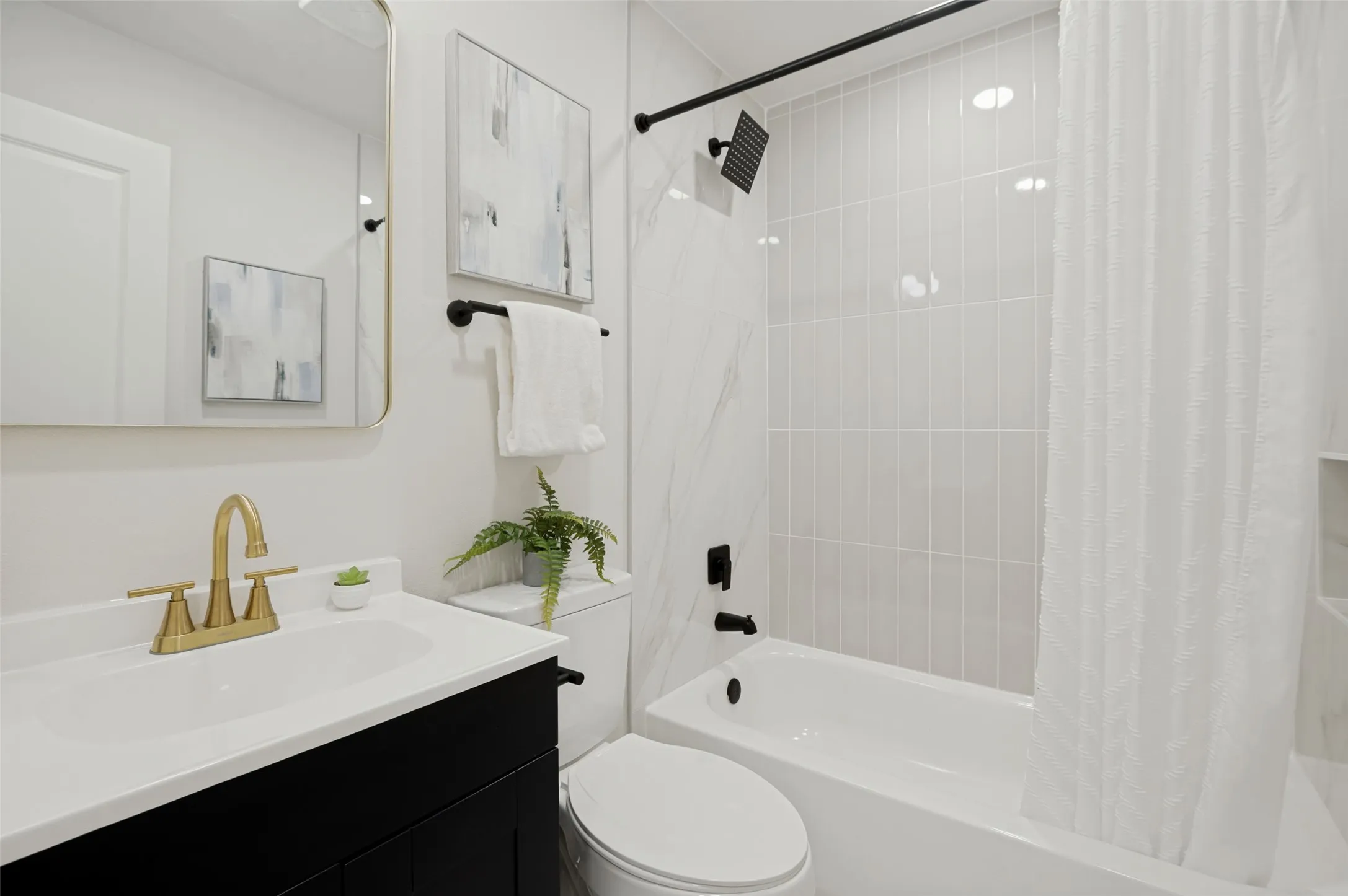 Bathroom featuring a single vanity with gold-tone faucet, a built-in bathtub with shower, and white tile surround