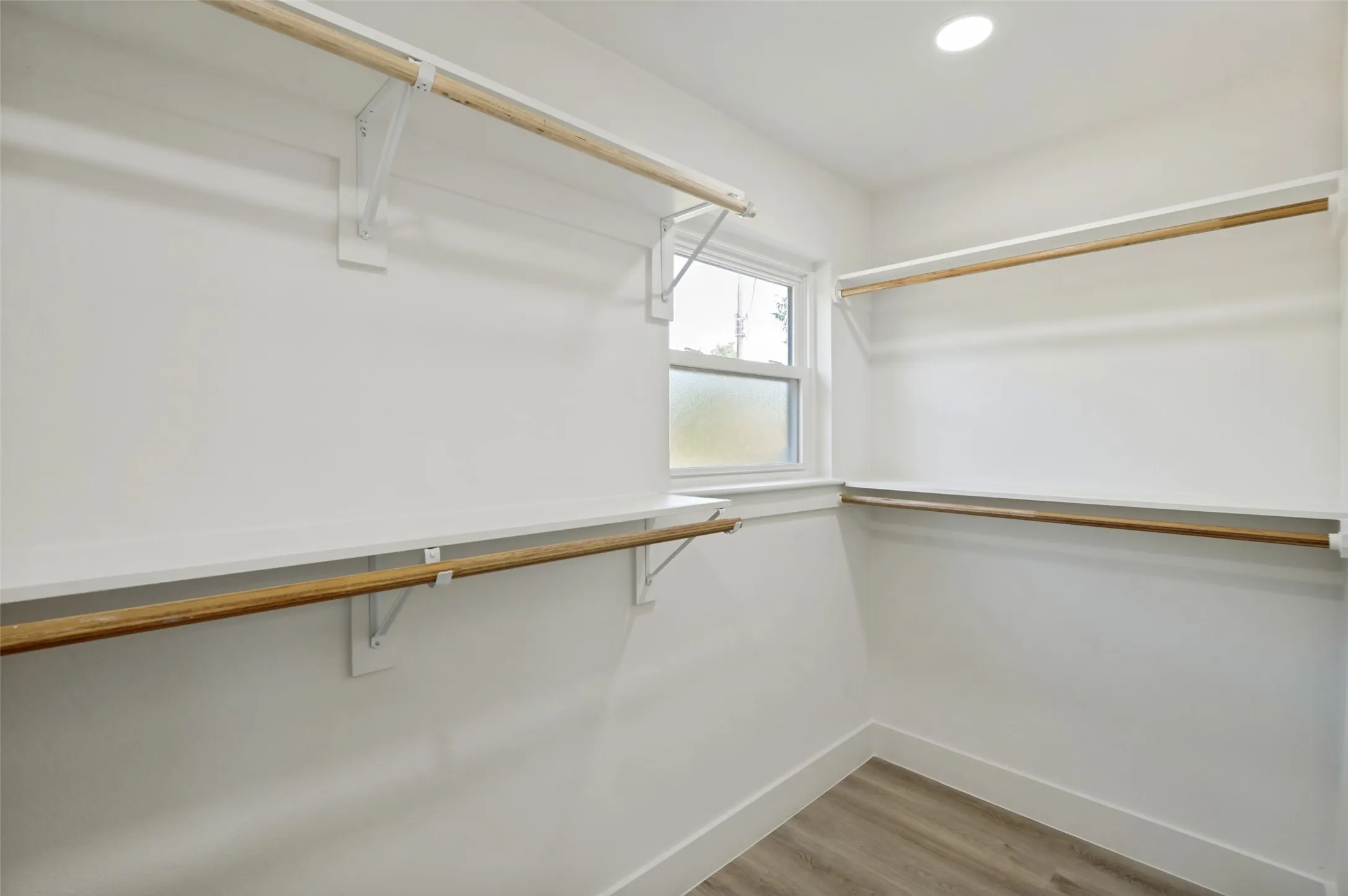 Walk-in closet featuring wood-finish flooring, recessed lighting, built-in shelving, and a window with privacy glass