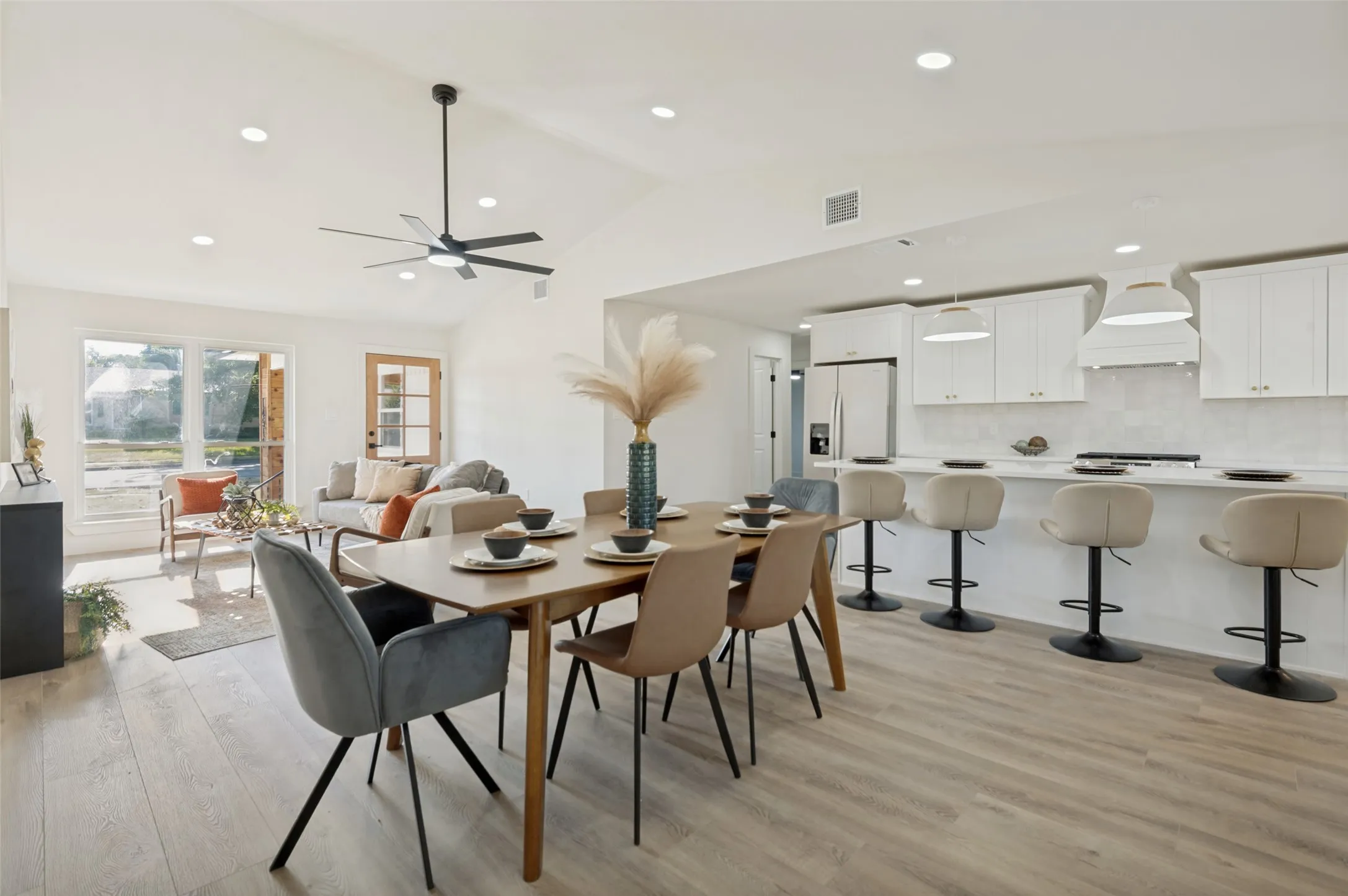Vaulted ceiling with recessed lighting and a ceiling fan, wood-finish flooring, white shaker cabinetry, an extended kitchen island with pendant lighting, and multiple large windows